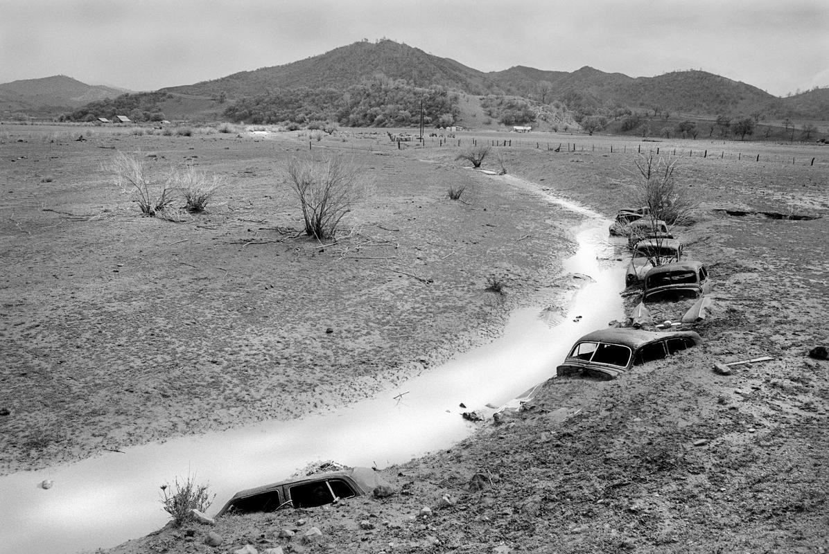 USA. CALIFORNIA. On the Doc Bar Ranch is a line of 40 year old Cadillacs half buried in the ground. They are exactly following the line of the San Adreas Fault and one of the few visible signs of exactly where the fault lies. They have now become a local tourist attraction and have been elevated to become works of art. Actually they were put there to protect the bank of the small river. 1991.