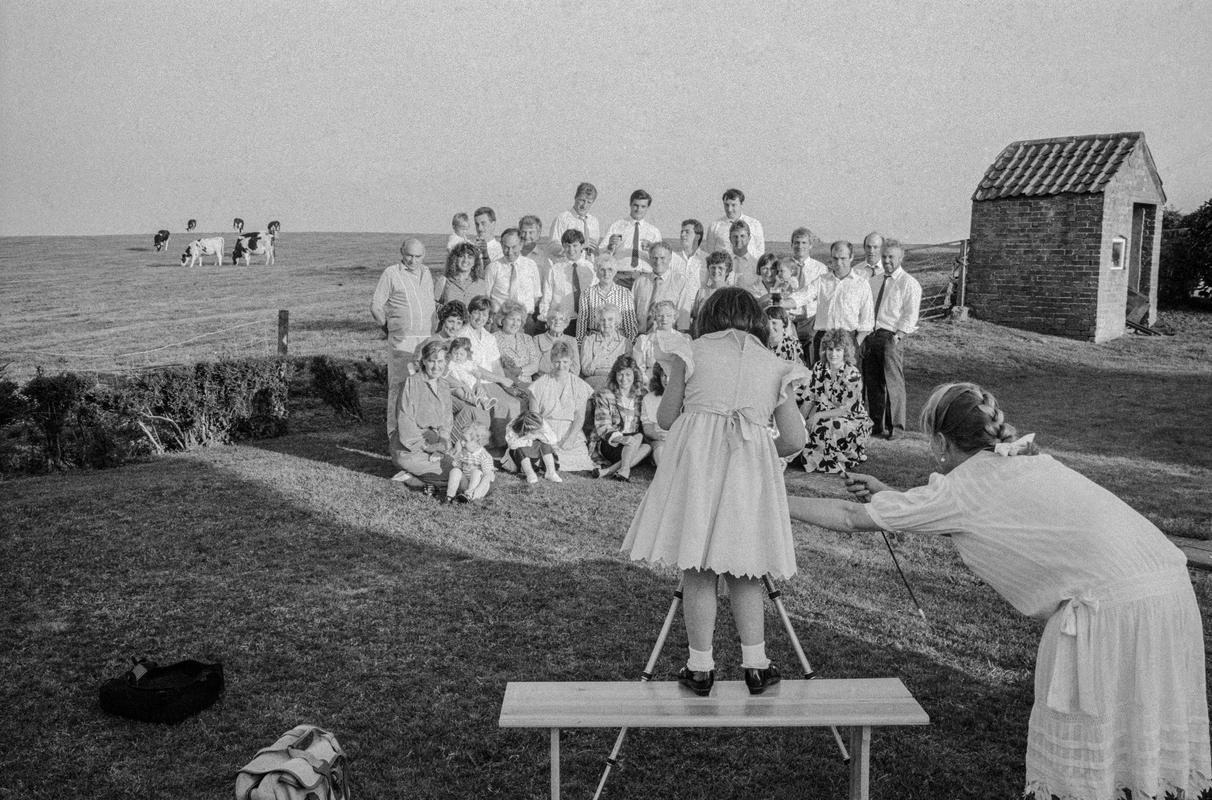 GB. WALES. Castleton. A large farming family pose as one of the junior members take their photograph under the guidance of the photographer Sue Packer. The family get together at least once a year for a party ( in this case for a Christening). A roast pig is traditionally the food every year. 1987