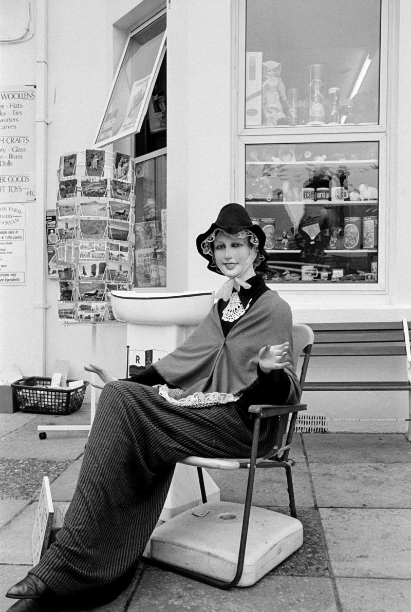 GB. WALES. Tenby.  General.  Mannequin in traditional Welsh costume. The march towards tourism is symbolised by the arificial Welsh mannequin wearing the Welsh traditional costume designed by an English woman Lady Llanover in the 19th century.  She drew on English fashions and a romantic imagination to create a national costume that had never existed in this form. 1989