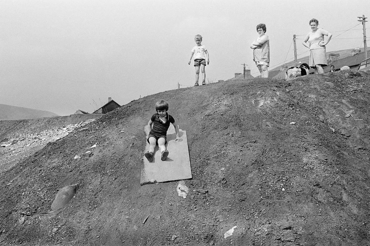 GB. WALES. Abertillery. Children make a wooden board into a sledge to slide down a slag tip side. 1977.