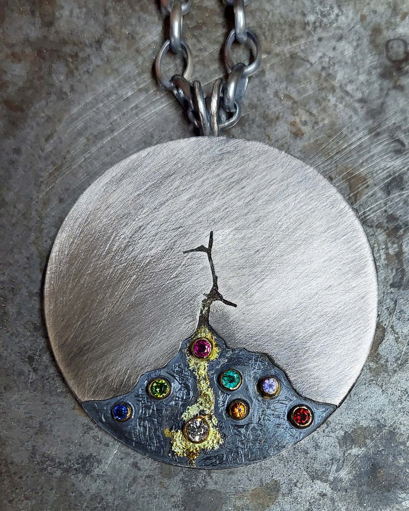 A circular silver pendant on a chain, placed on a grey stone background