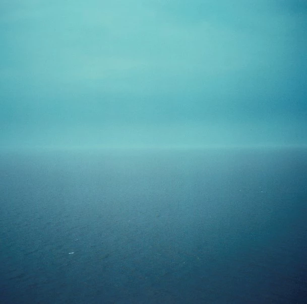 A square photograph of a blue sky above a blue sea in misty weather.