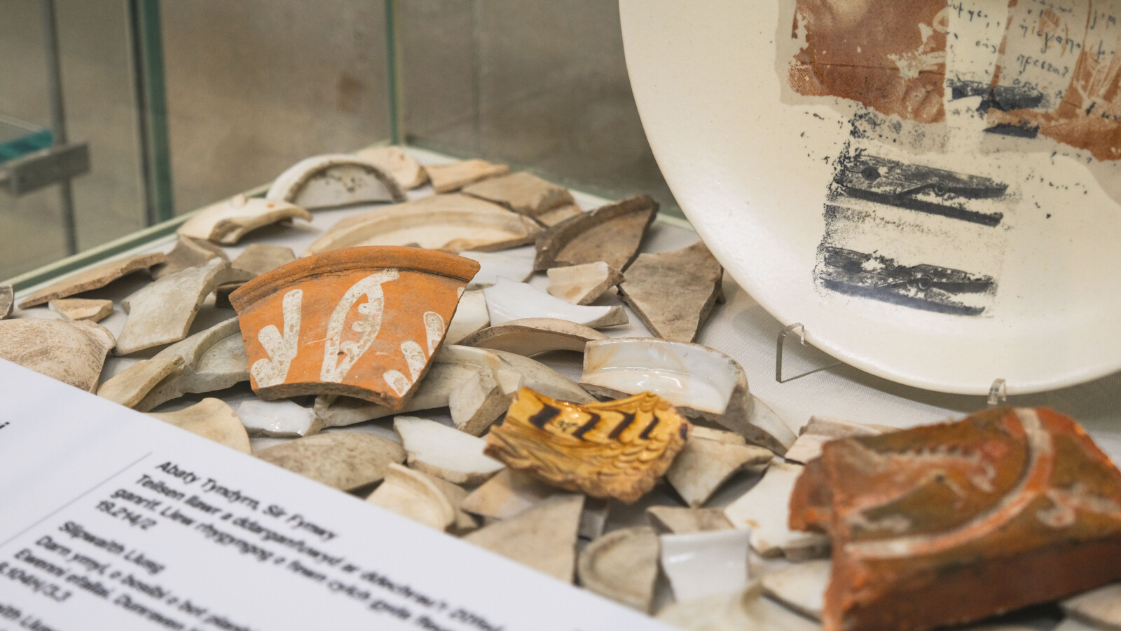 Close-up of a collection of decorated pottery shards in a display case in a museum, with a label below.