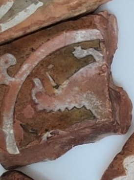 A pottery fragment with a motif of an animal inside a circle, with a hooked shape projecting out of the circle at the corner of the tile.