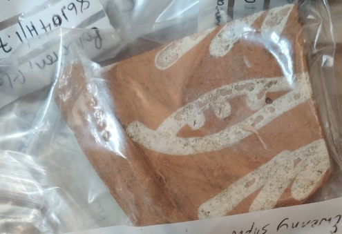 A sealed transparent plastic bag containing a pottery shard, with a label for identification.