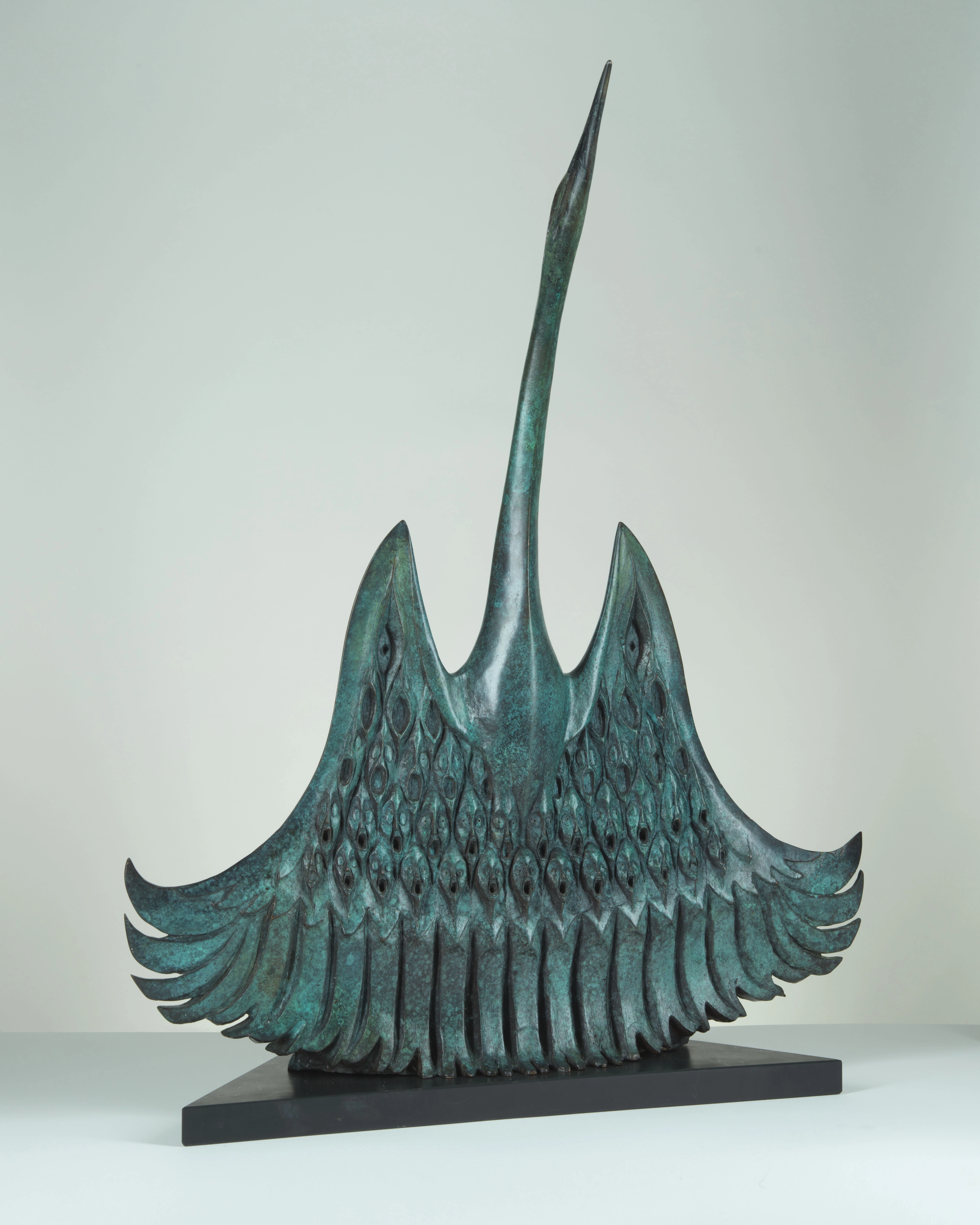 Bronze sculpture in a light blue shade showing a bird with faces under its wings.