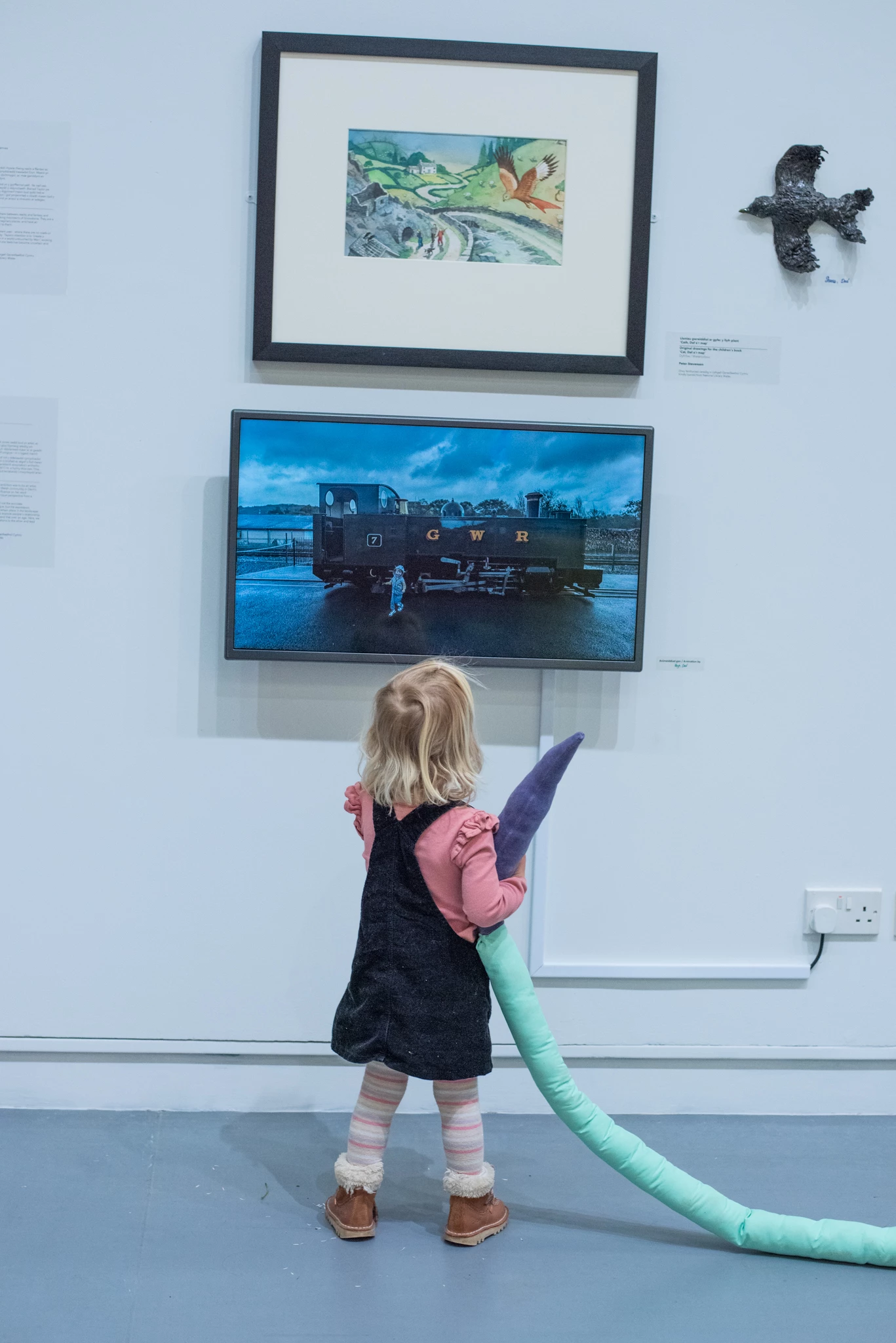 A young child looks up at a screen and an artwork on a gallery wall. She is totally engrossed in what's in front of her.