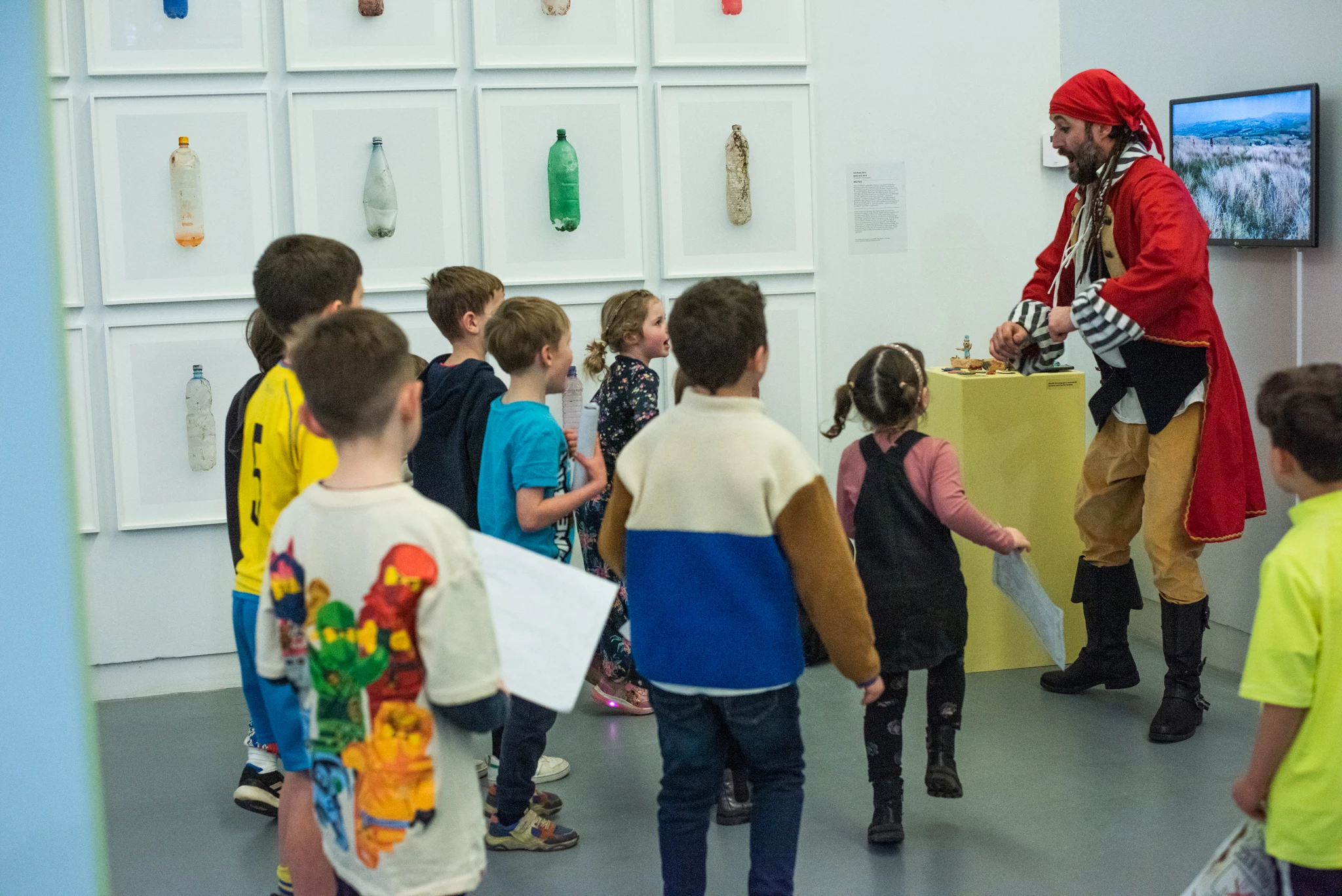 A man dressed as a pirate entertains children in a gallery space.