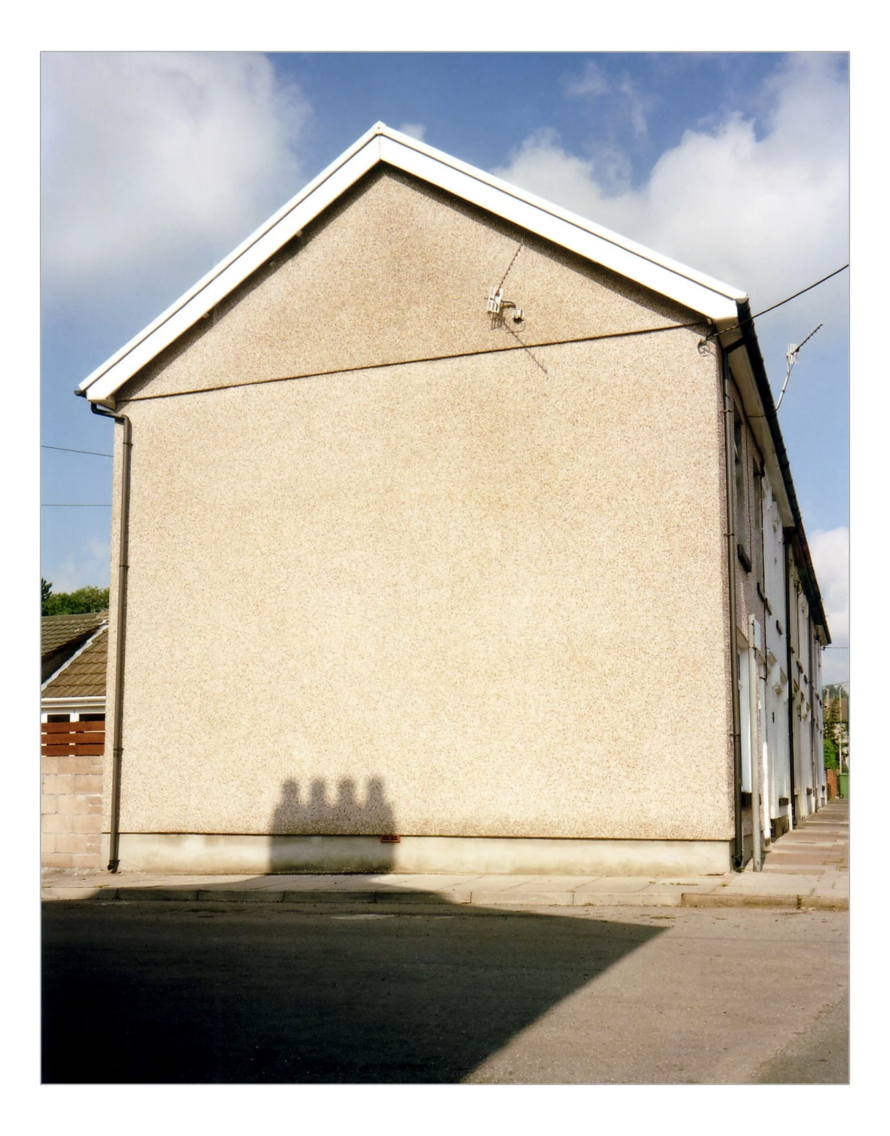 The side of an end house on a Valleys terraced street. The house is a light grey colour in pebble dash and has a television aerial sticking out.