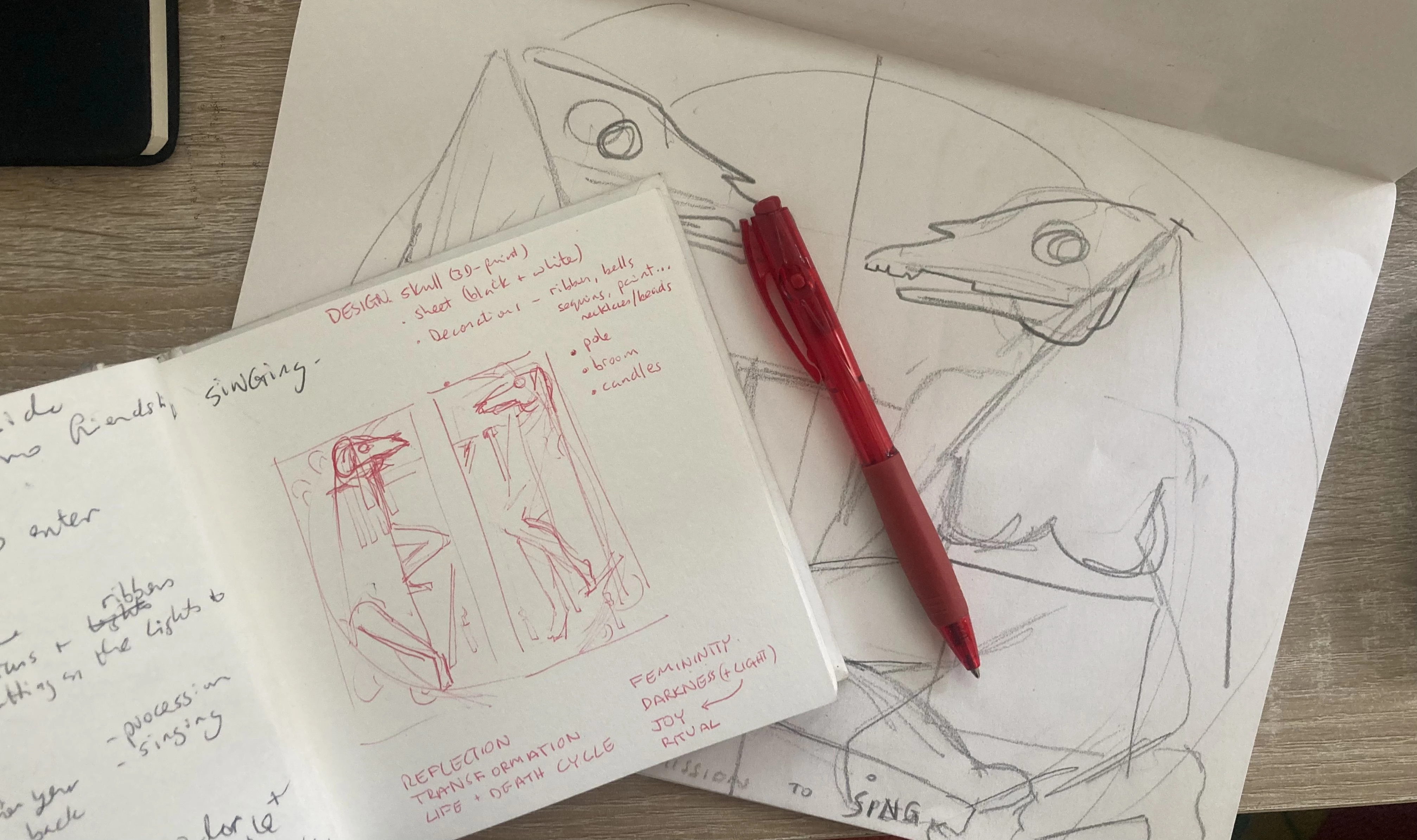 Open sketchbook and pen resting on larger paper.