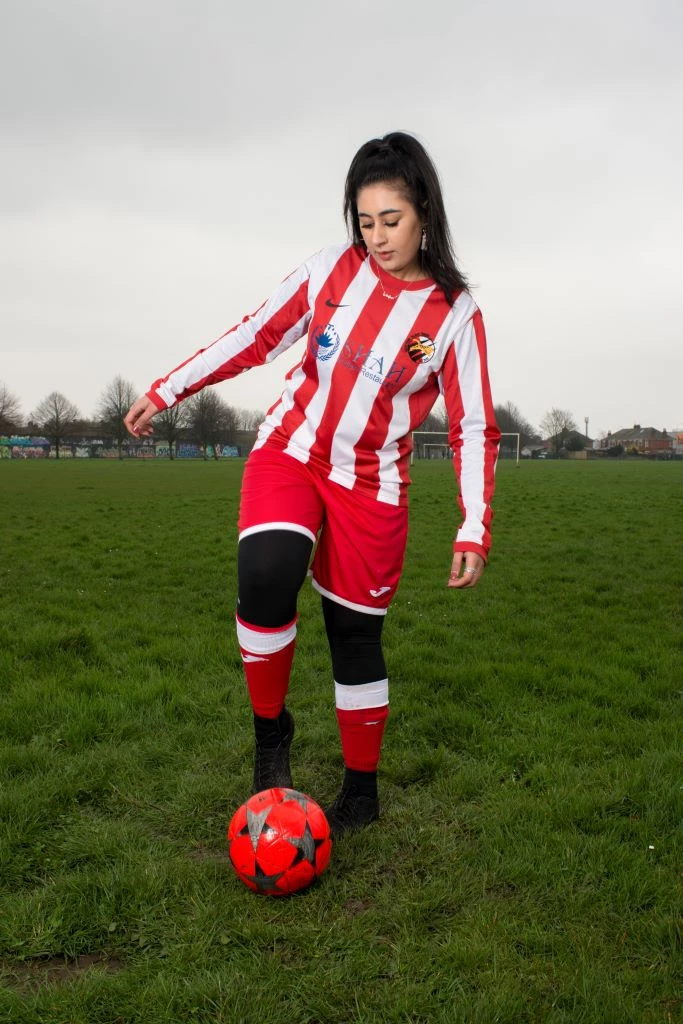 A woman plays football on a football field, she wears a full football kit.