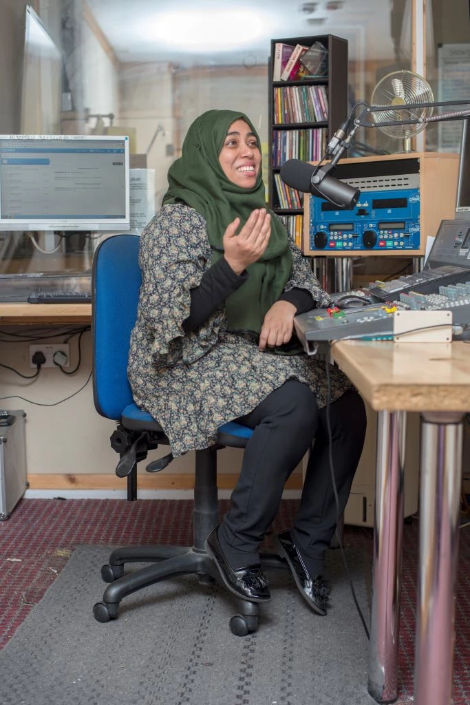 A woman sits at a microphone in a recording studio