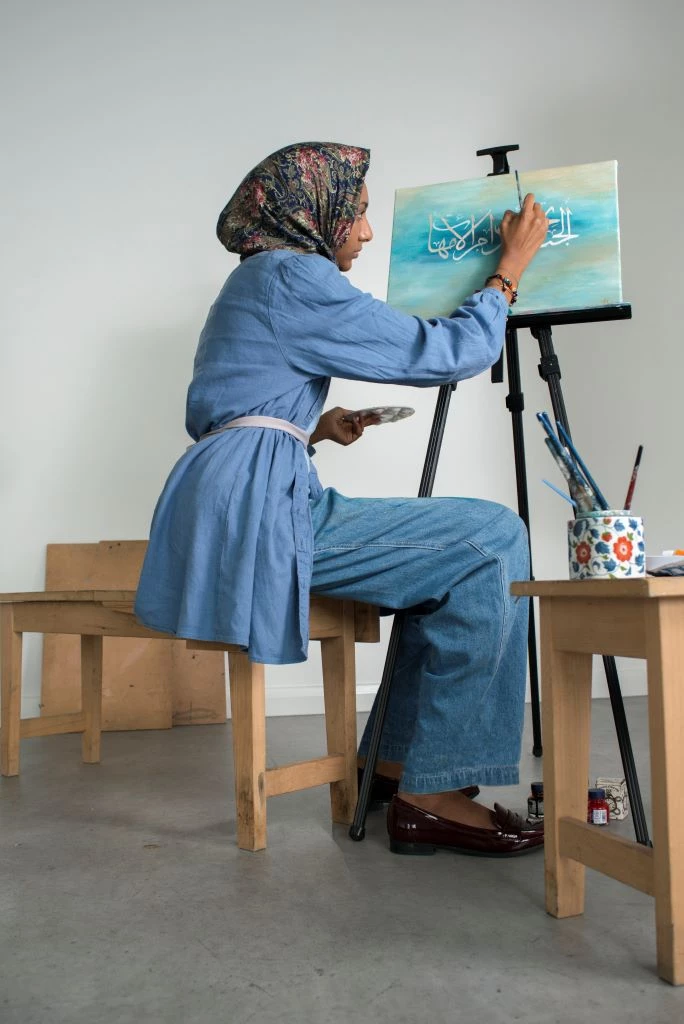 An artist sits in front of her easel, working on her painting.