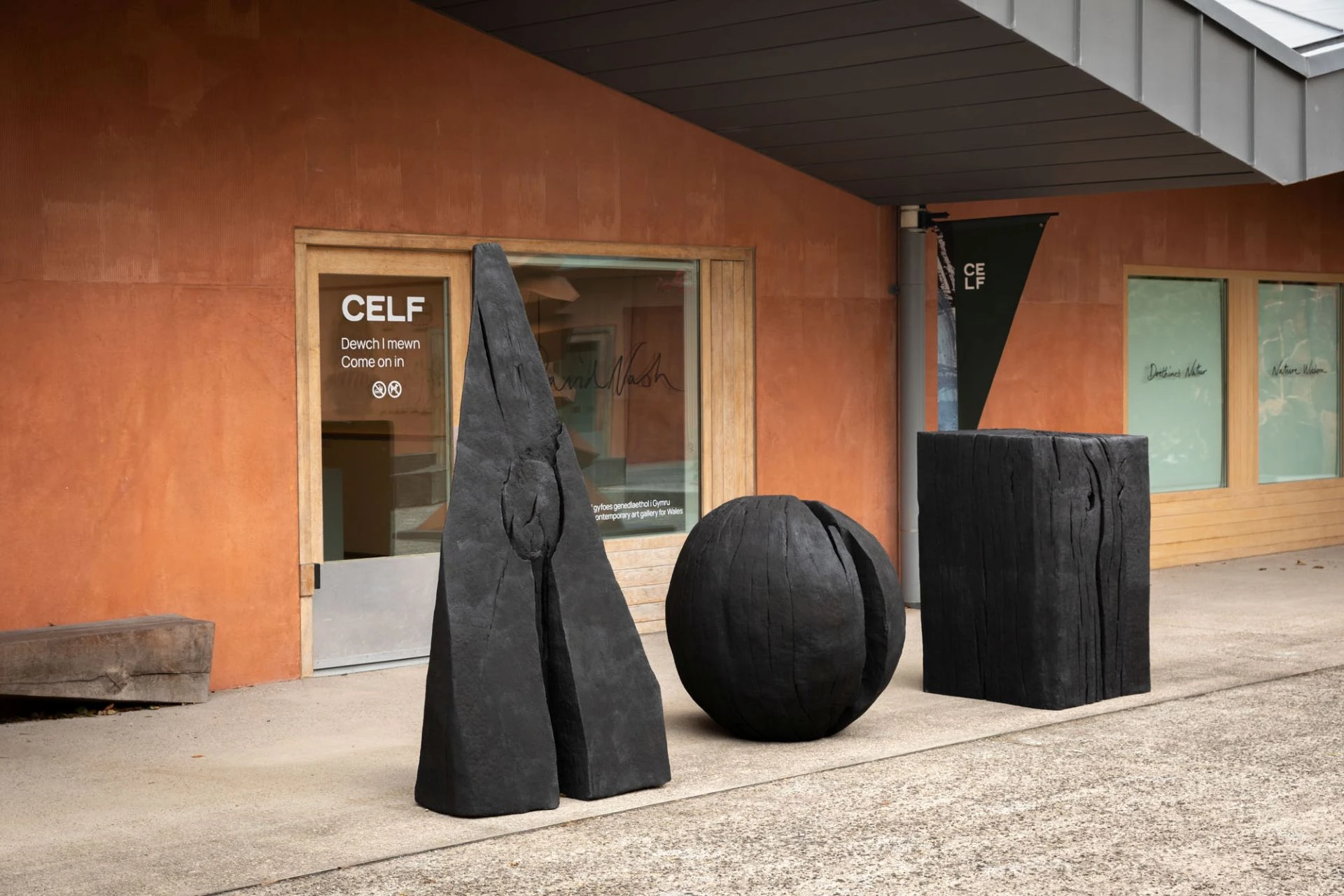 Courtyard of Ruthin Craft Centre. Three charred wooden sculptures - one pyramid, one sphere and one cube - are placed in front of the gallery.