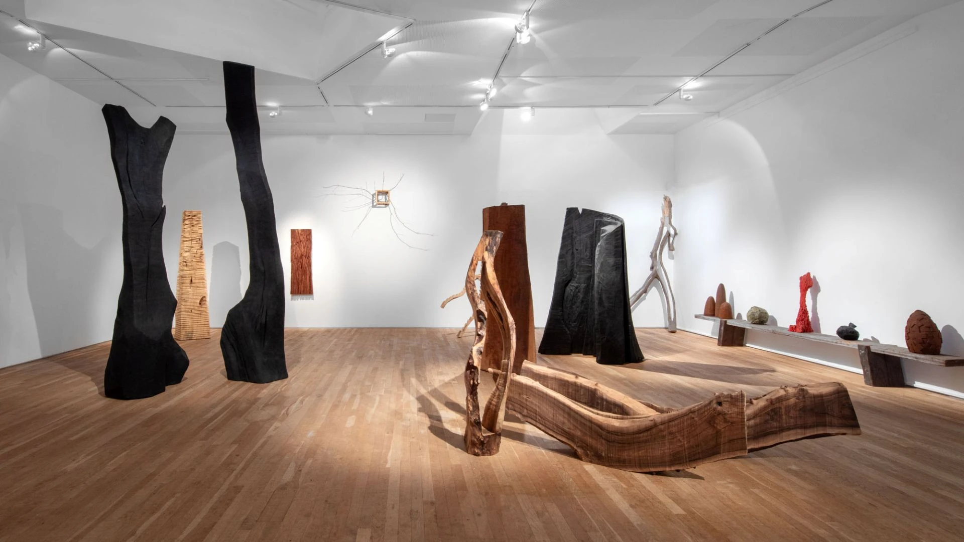 Gallery space filled with wooden sculptures of all kinds. Some are charred black.